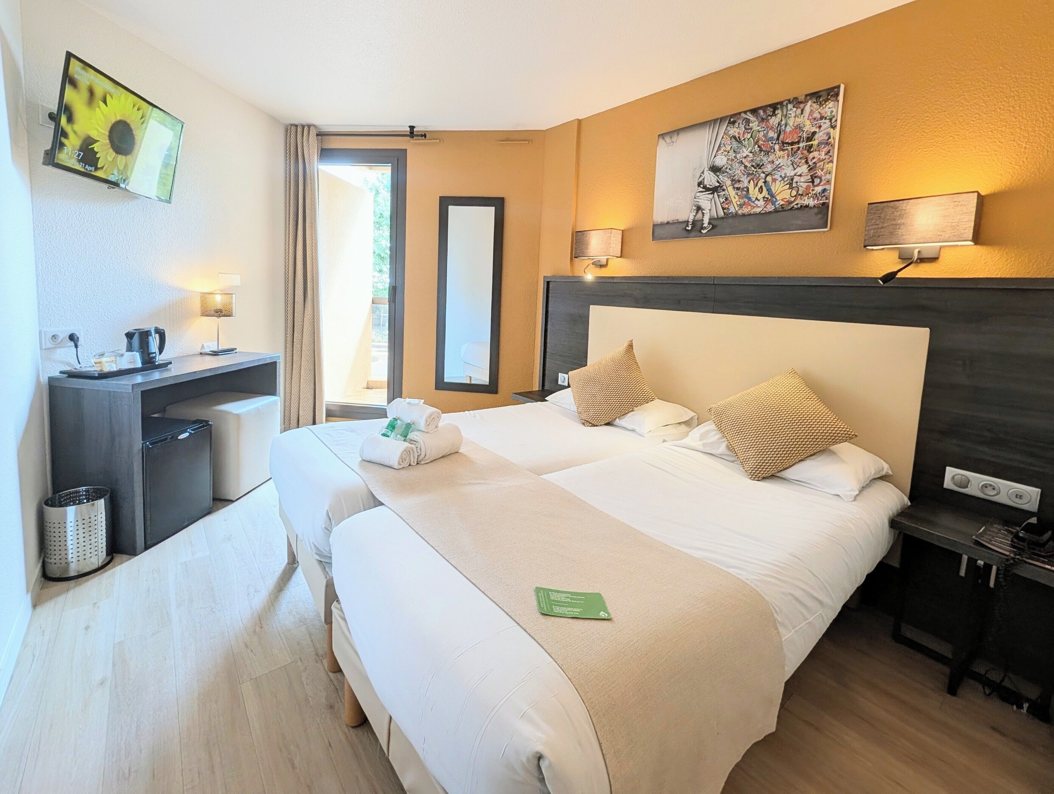 Ein Hotelzimmer mit Bett, Nachttischen, Schreibtisch, Stuhl, Lampe, einem Bild und einem Fenster.