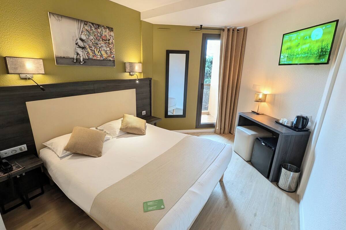 Una habitación de hotel con cama, mesitas de noche, escritorio, televisión y vistas al exterior.