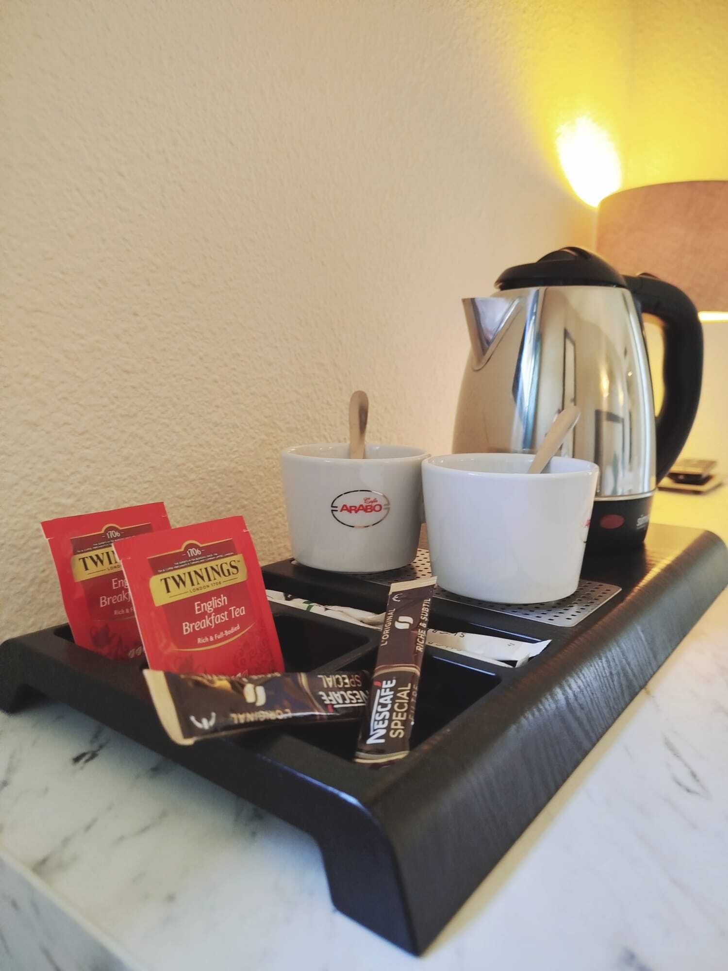 A tray with Twinings English Breakfast Tea, a white cup, a spoon, and a black and silver electric kettle.