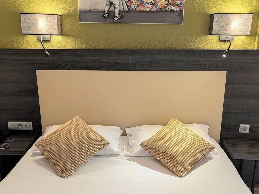 A hotel room with a large bed, two bedside lamps, a wall-mounted artwork, and a dark wood headboard.