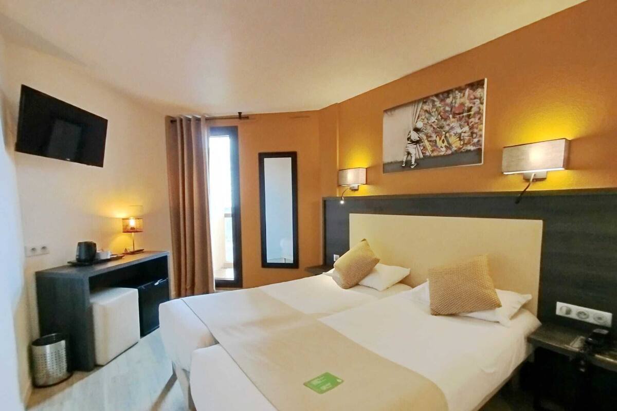 Una habitación de hotel con una cama grande, lámparas de noche, televisión, escritorio y espejo.