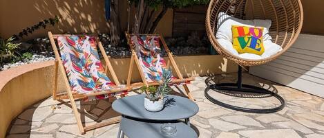 Un espace extérieur aménagé avec deux fauteuils de jardin, une petite table et une chaise en osier.