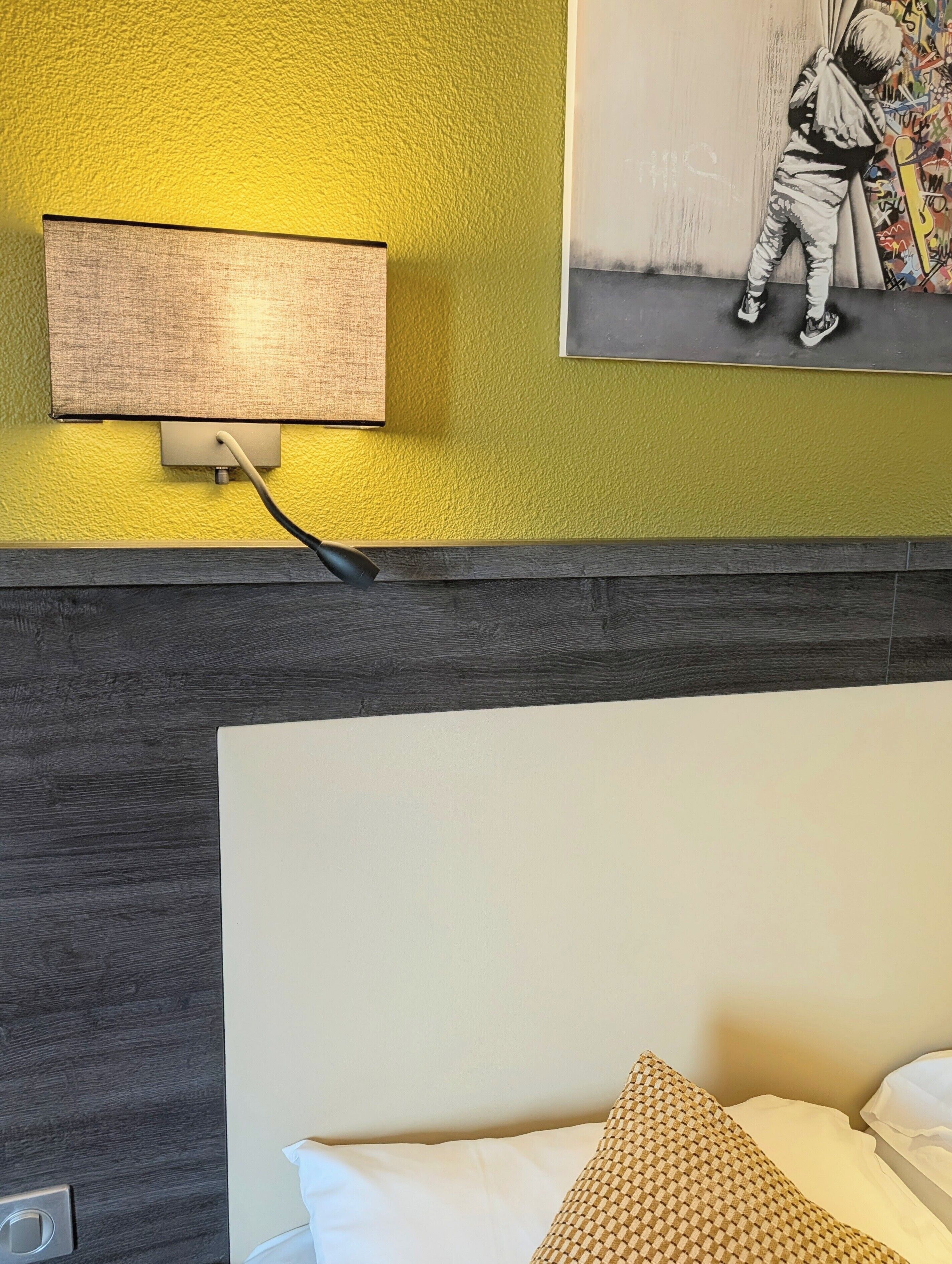 Quarto de hotel com uma cama, uma luminária de parede e um quadro.