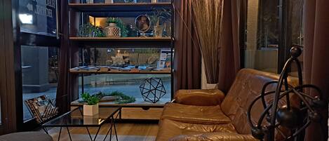 Un salon chaleureux avec un canapé en cuir marron, une table basse en bois et une bibliothèque remplie d’objets décoratifs et de plantes.
