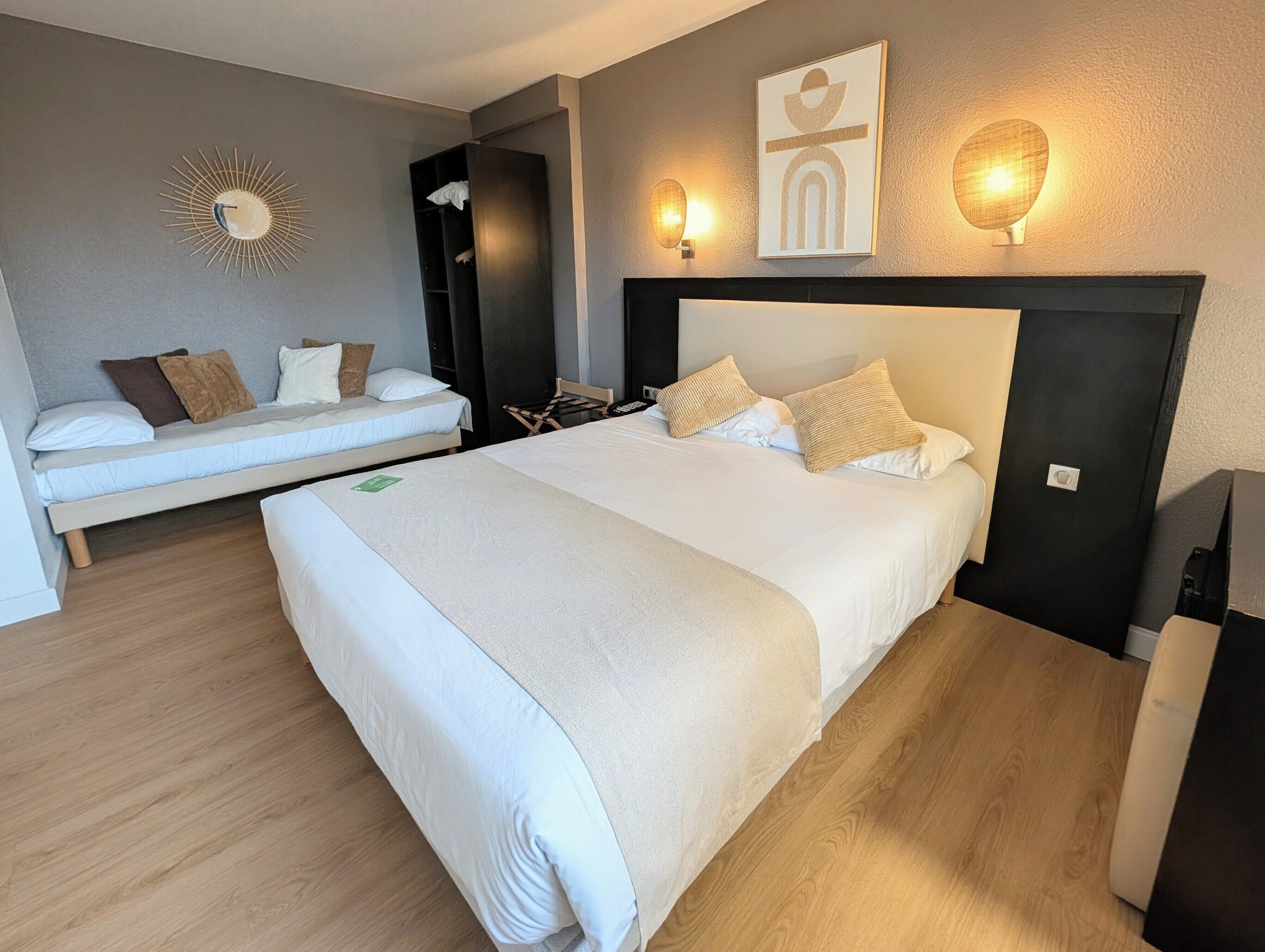 A bedroom with a large bed, a smaller bed, a wardrobe, a wall-mounted light, and a decorative wall piece.