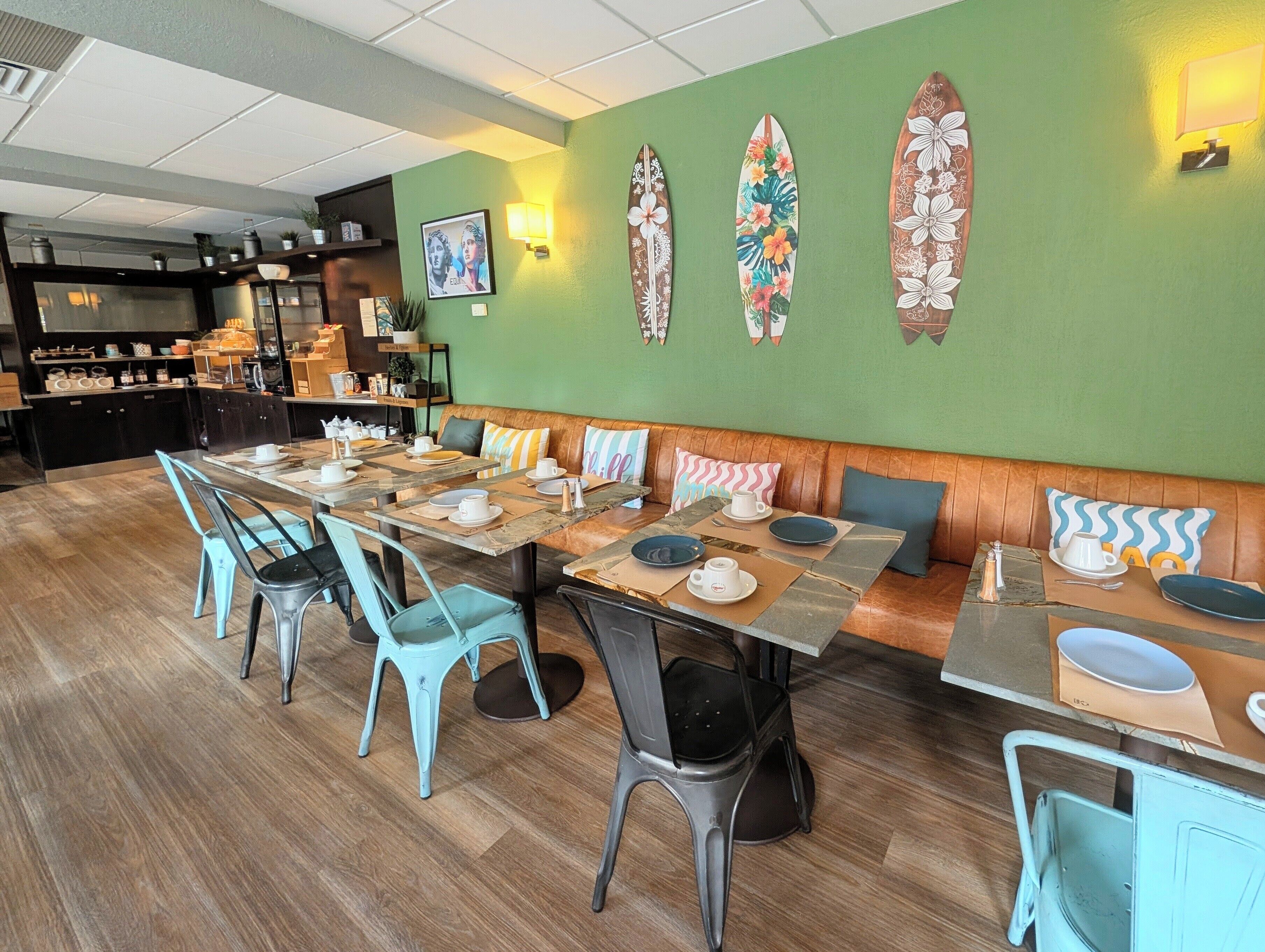 Un restaurante con una larga mesa de madera, sillas color turquesa y una pared verde decorada con tablas de surf.