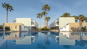 A pool with clear reflections of palm trees and modern buildings. - Apollon Windmill Hotel (Kos)