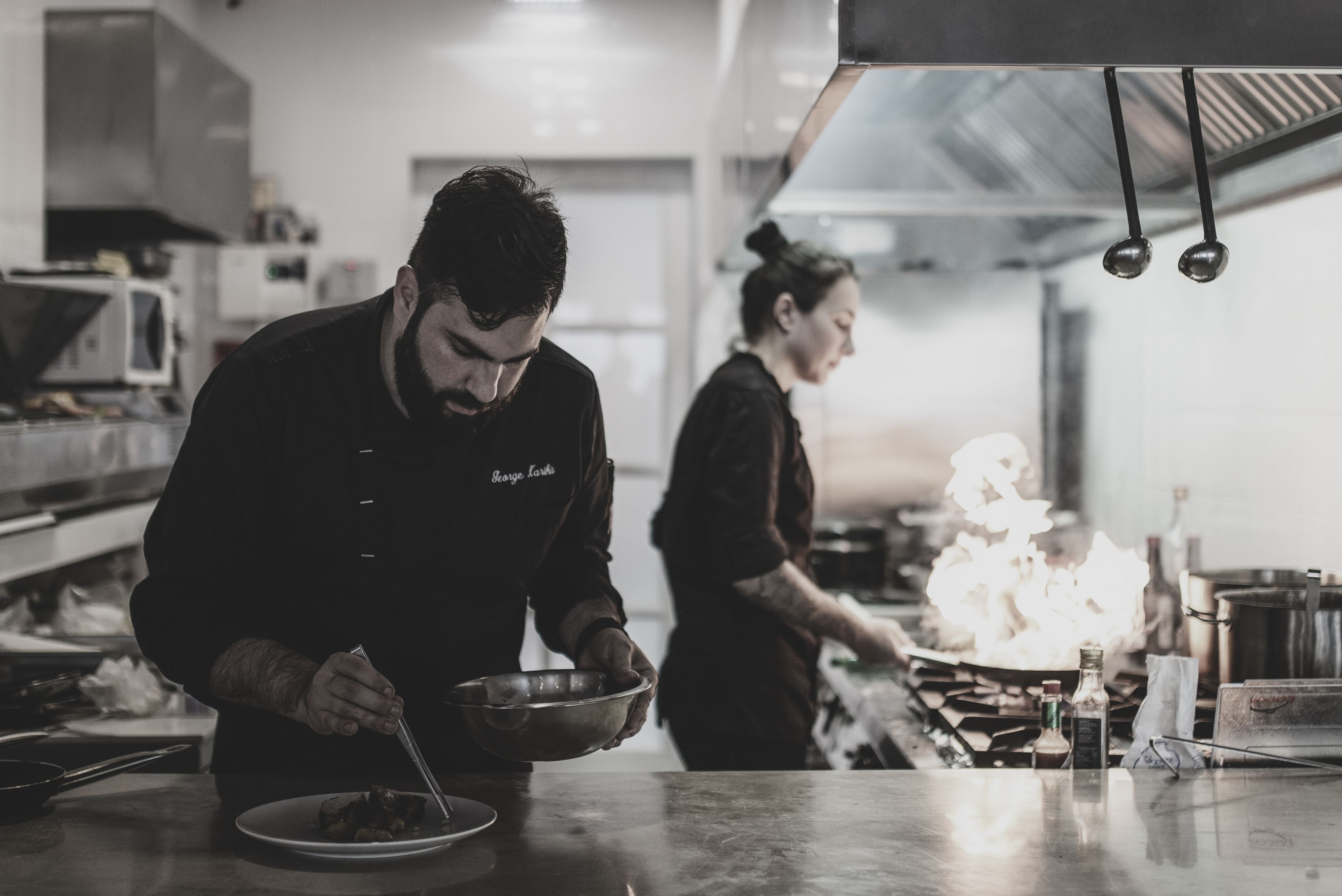 A chef preparing food in a professional kitchen with stainless steel appliances and a clean, organized layout.