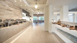 A modern kitchen area with a long counter, multiple sinks, and a variety of food items displayed. - Apollon Windmill Hotel (Kos)