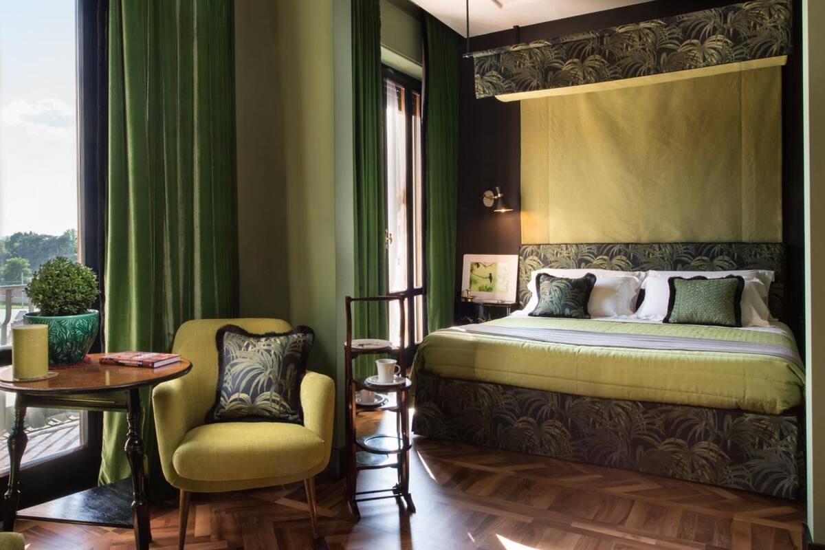 A hotel room with a bed, a chair, a small table, and a view of the outdoors.