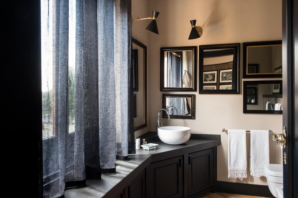 A modern bathroom with a large window, dark cabinetry, a white sink, and multiple mirrors. - Velona's Jungle Luxury Suites (Florence)