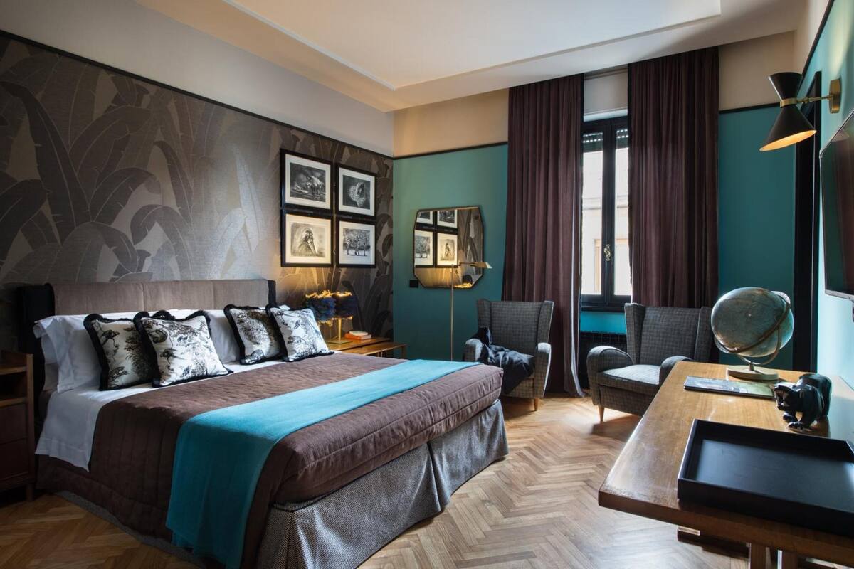 A hotel room with a large bed, two armchairs, a desk with a globe, and a wall with framed pictures.