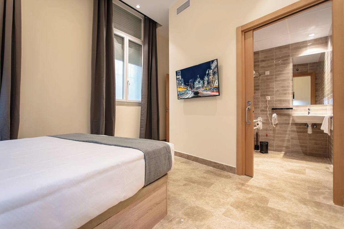 A hotel room with a bed, a painting, a bathroom with a sink and mirror, and a shower.