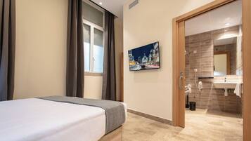 A hotel room with a bed, a painting, a bathroom with a sink and mirror, and a shower.