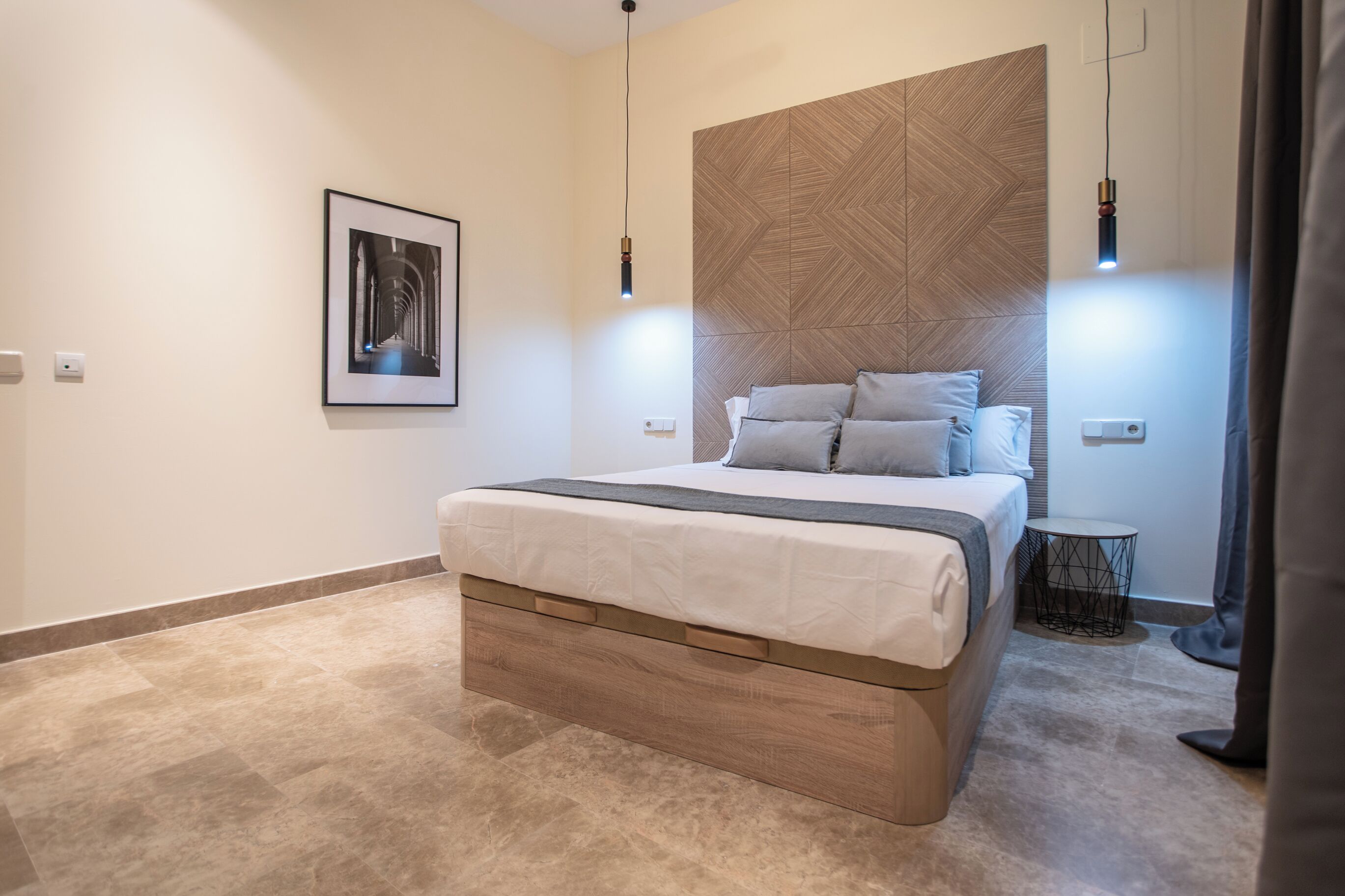 A modern bedroom with a bed, a wall-mounted picture, and a small side table.