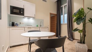 A modern kitchen with white cabinets, a microwave, a sink, and a dining area with a round table and chairs. - Suites You Opera (Madrid)