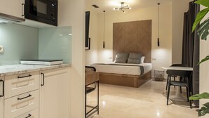 A modern kitchen with a microwave, a dining area with a table and chairs, and a bed with a headboard. - Suites You Opera (Madrid)