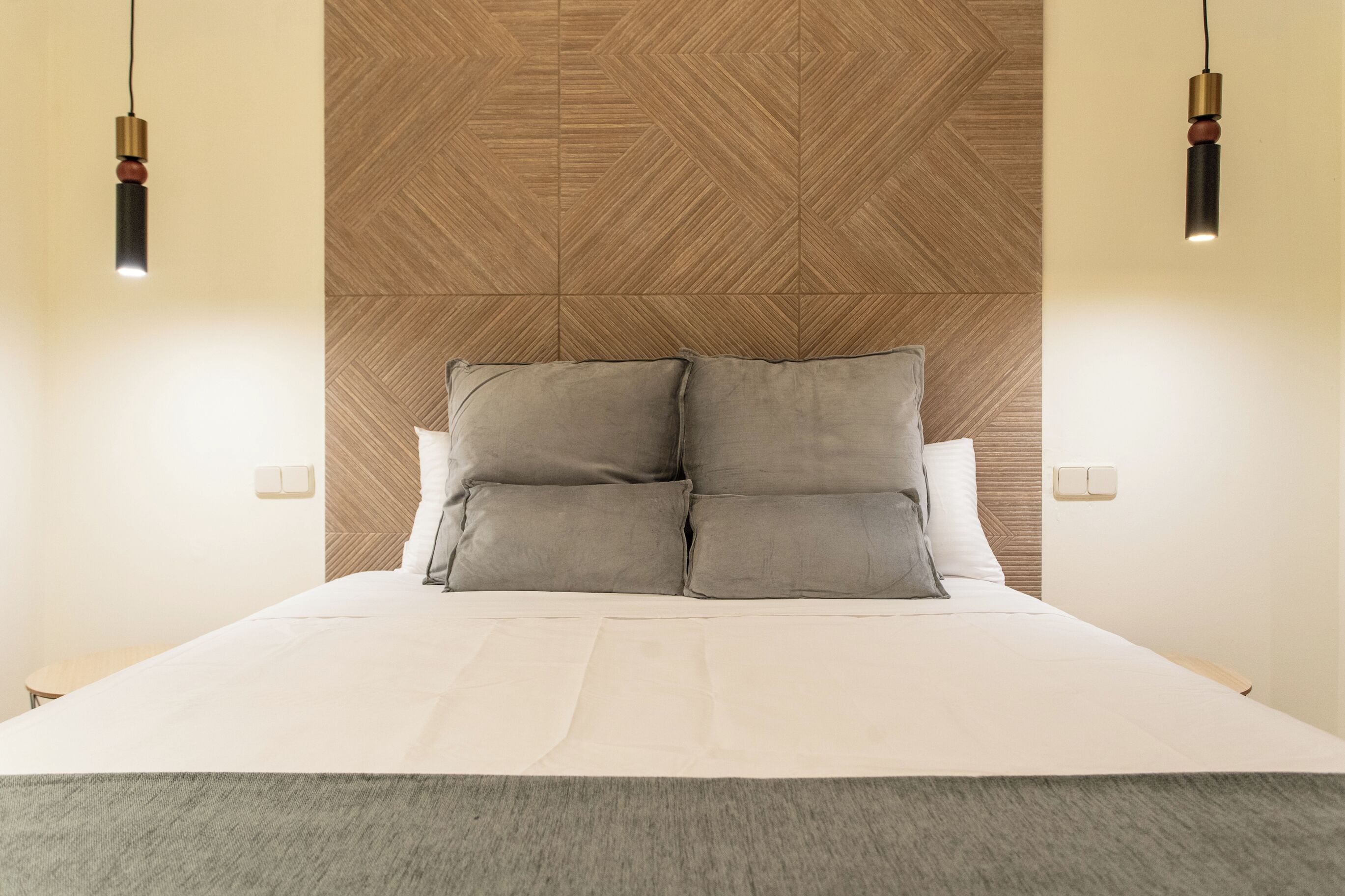 A modern bedroom with a large bed, two bedside tables, and a geometric-patterned headboard.