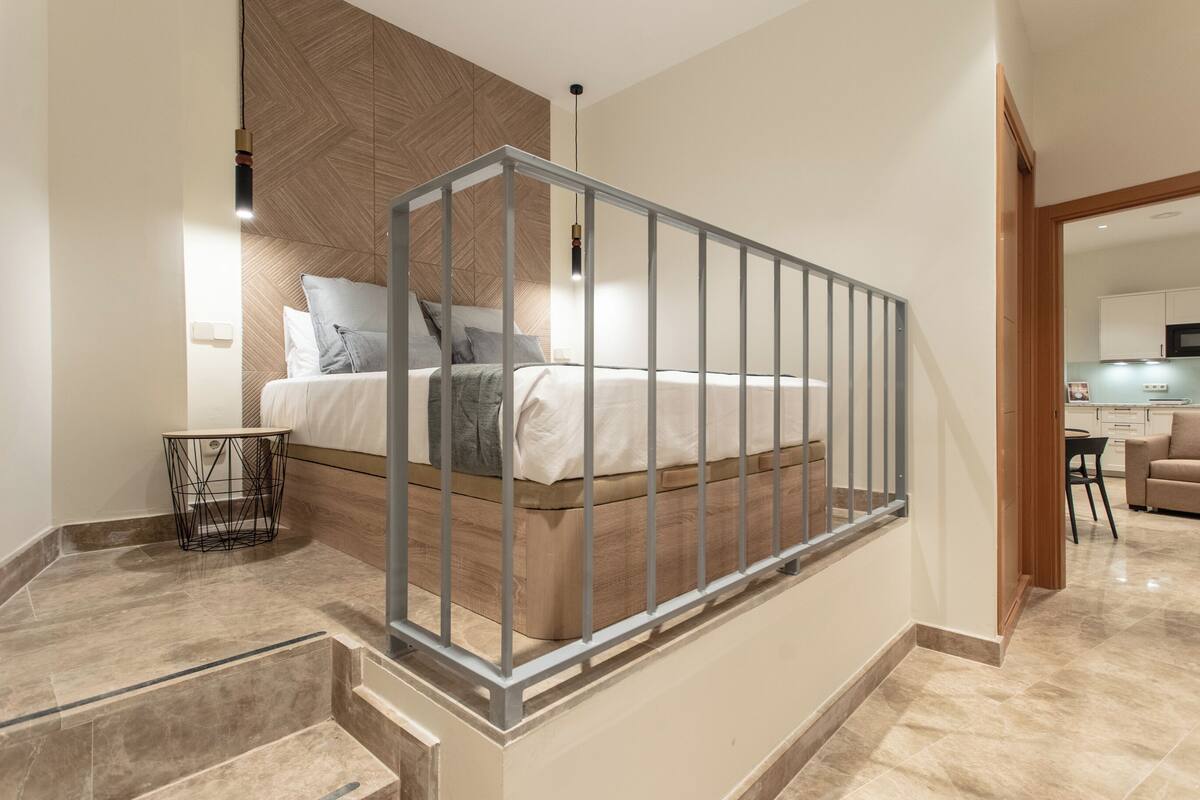 A modern bedroom with a wooden headboard, a metal railing, and a small bedside table.
