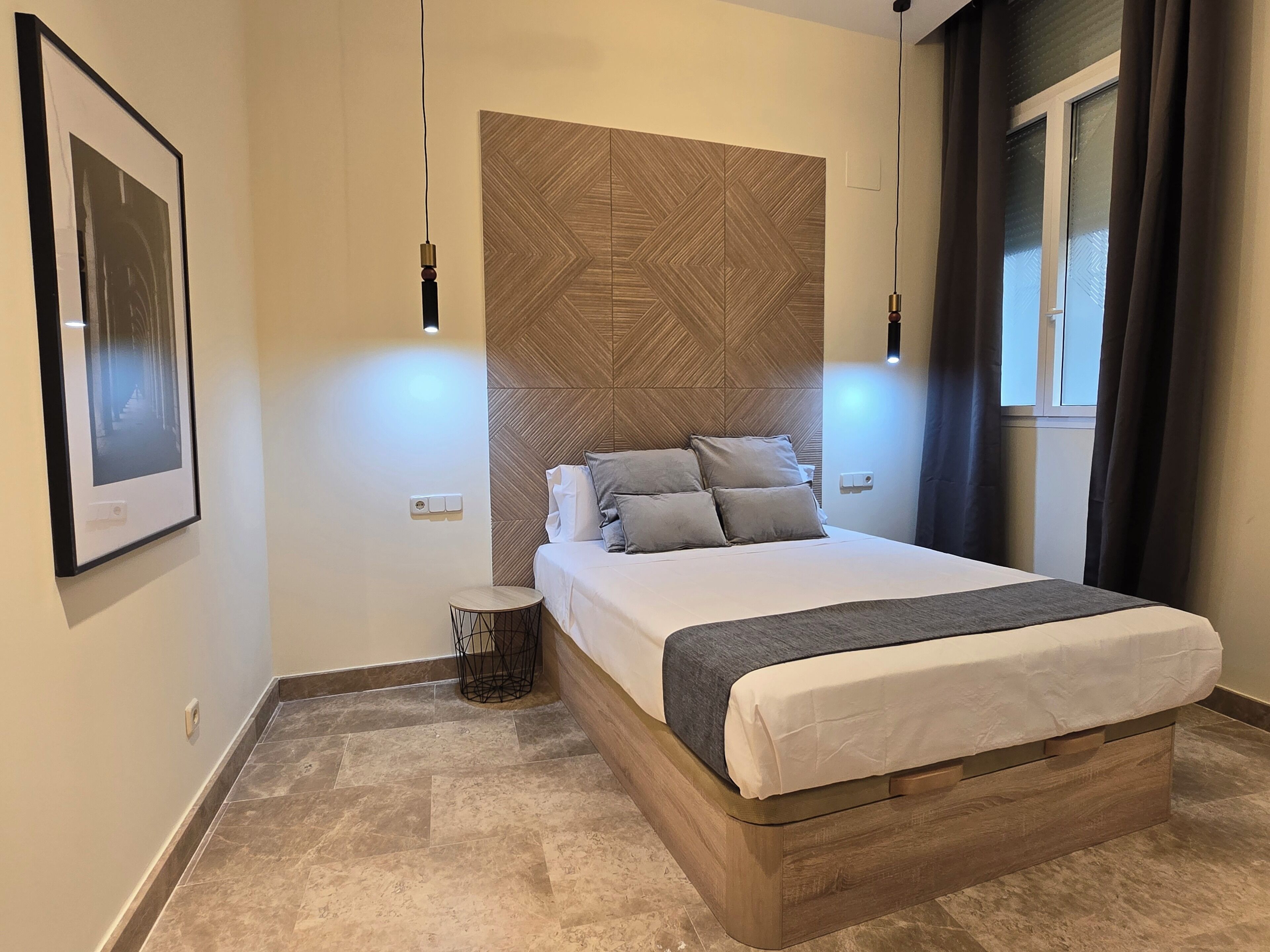Un dormitorio moderno con una cama, lámparas de noche, una mesita redonda y un cuadro enmarcado en la pared.