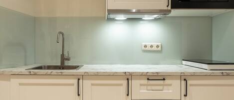A kitchen with a stainless steel sink, a microwave, and a countertop with a white marble-like surface.