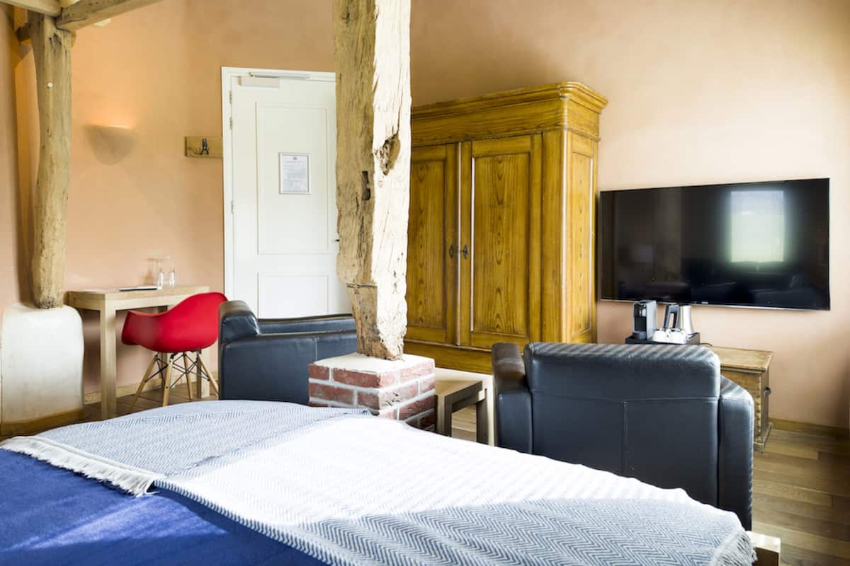Une pièce comprenant un lit, un téléviseur, une armoire en bois et une chaise rouge.