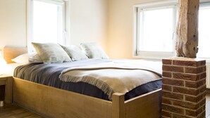 Un dormitorio con una cama de madera, una chimenea de ladrillo y vigas de madera a la vista en el techo.
