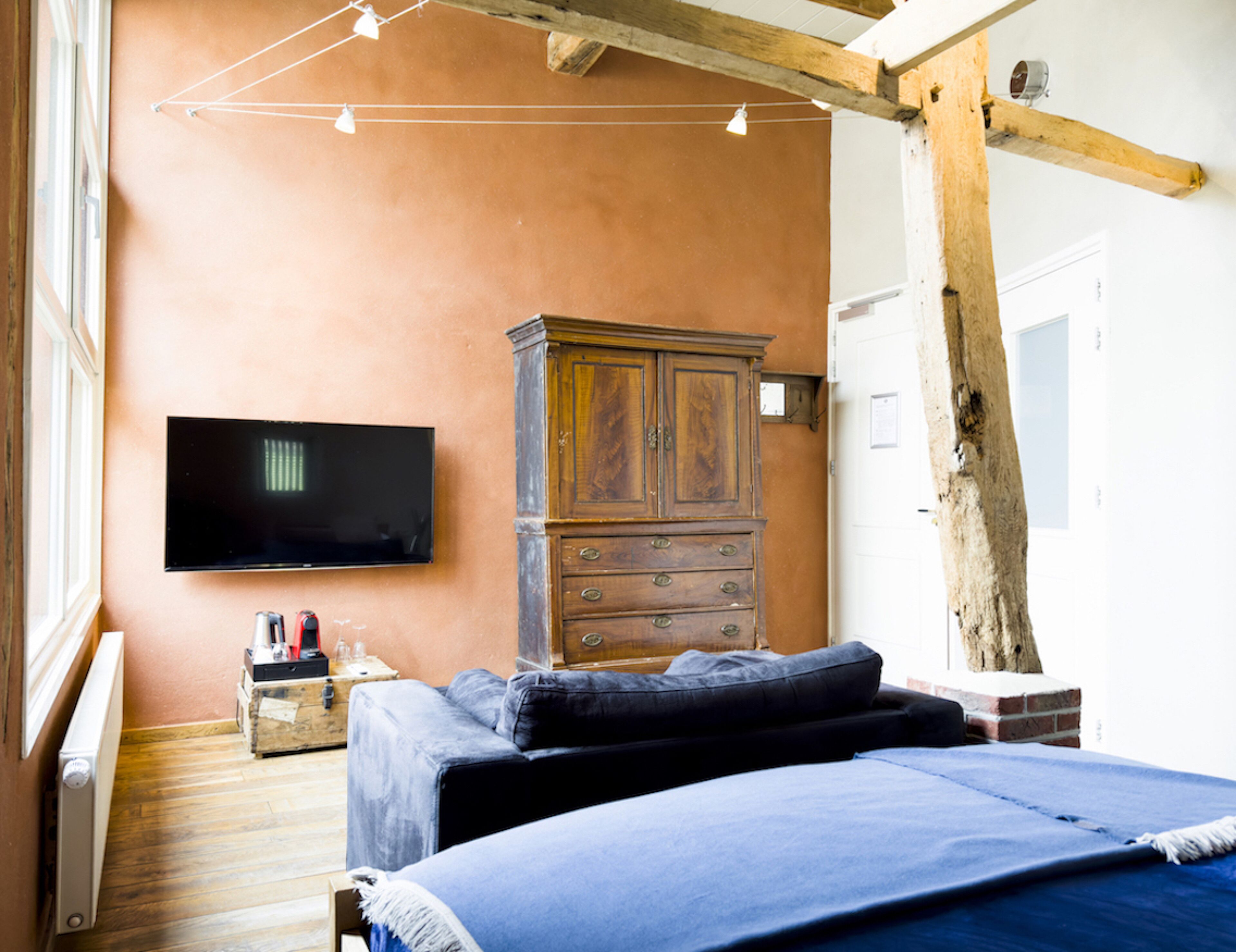 Een slaapkamer met een bed, een houten dressoir, een televisie en een raam.