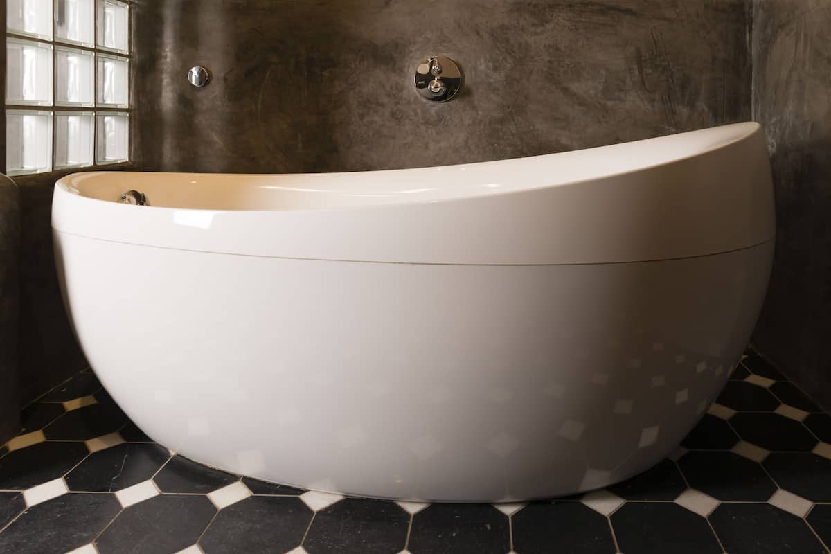 Une grande baignoire blanche, autoportante, dans une salle de bain dont le sol est carrelé et un des murs présente une texture particulière.