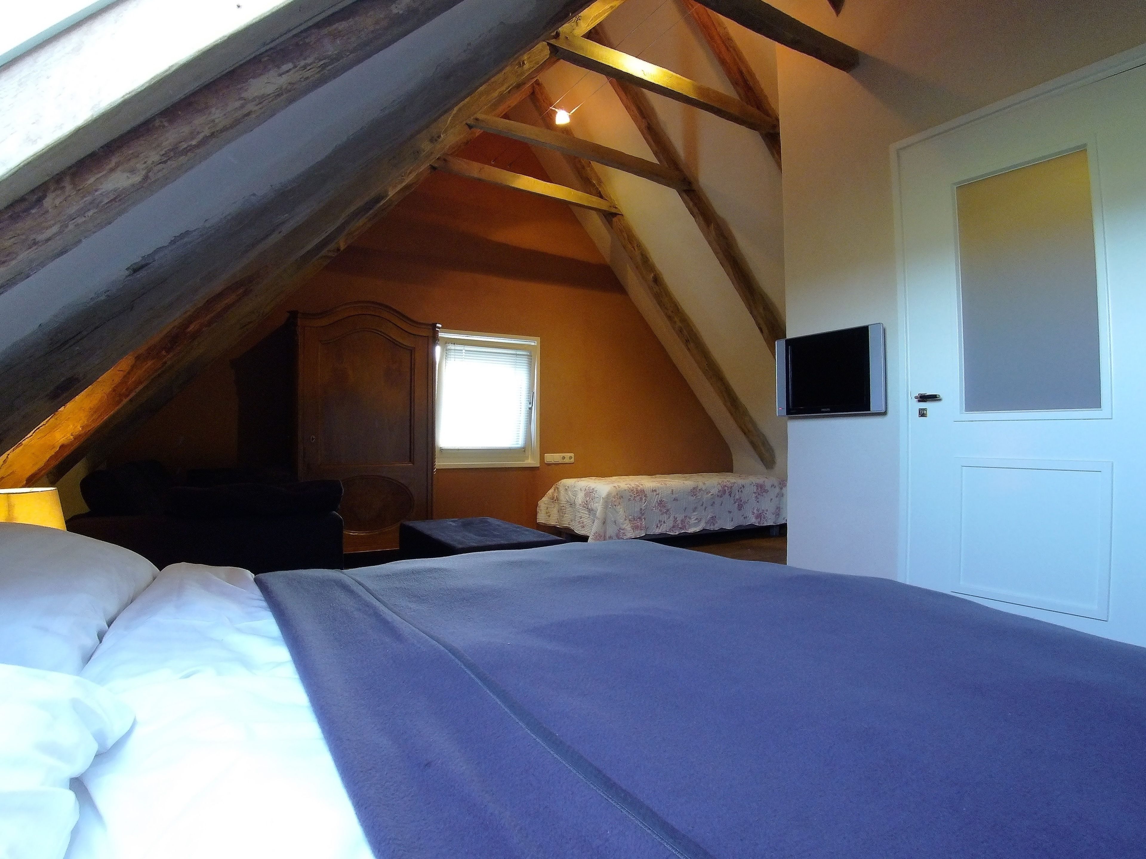 A bedroom with a sloped ceiling, a bed, a bedside table, a lamp, a window, and a door.