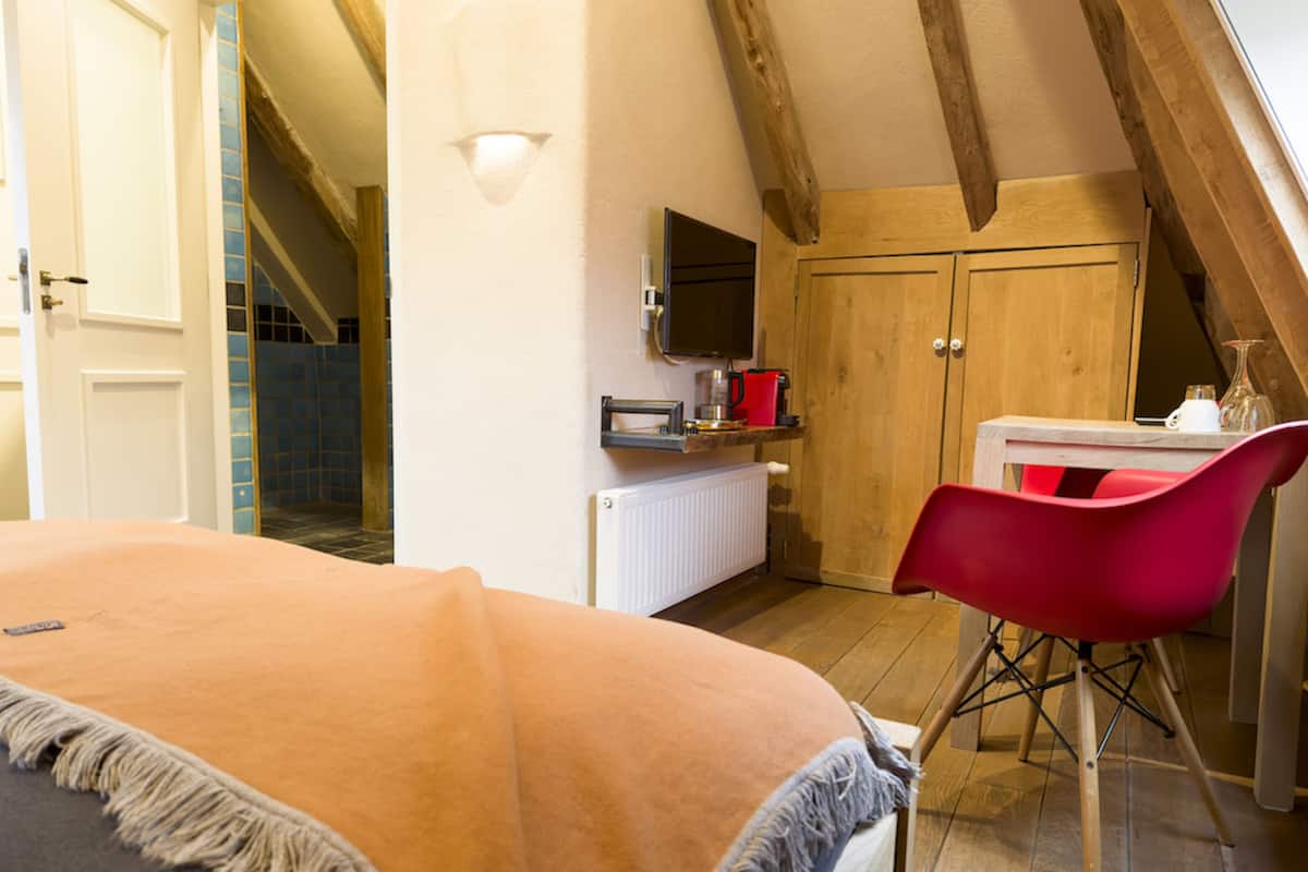 Une chambre à coucher comprenant un lit, un fauteuil rouge, un téléviseur, une armoire en bois et un coin cuisine avec une bouilloire et une machine à café.