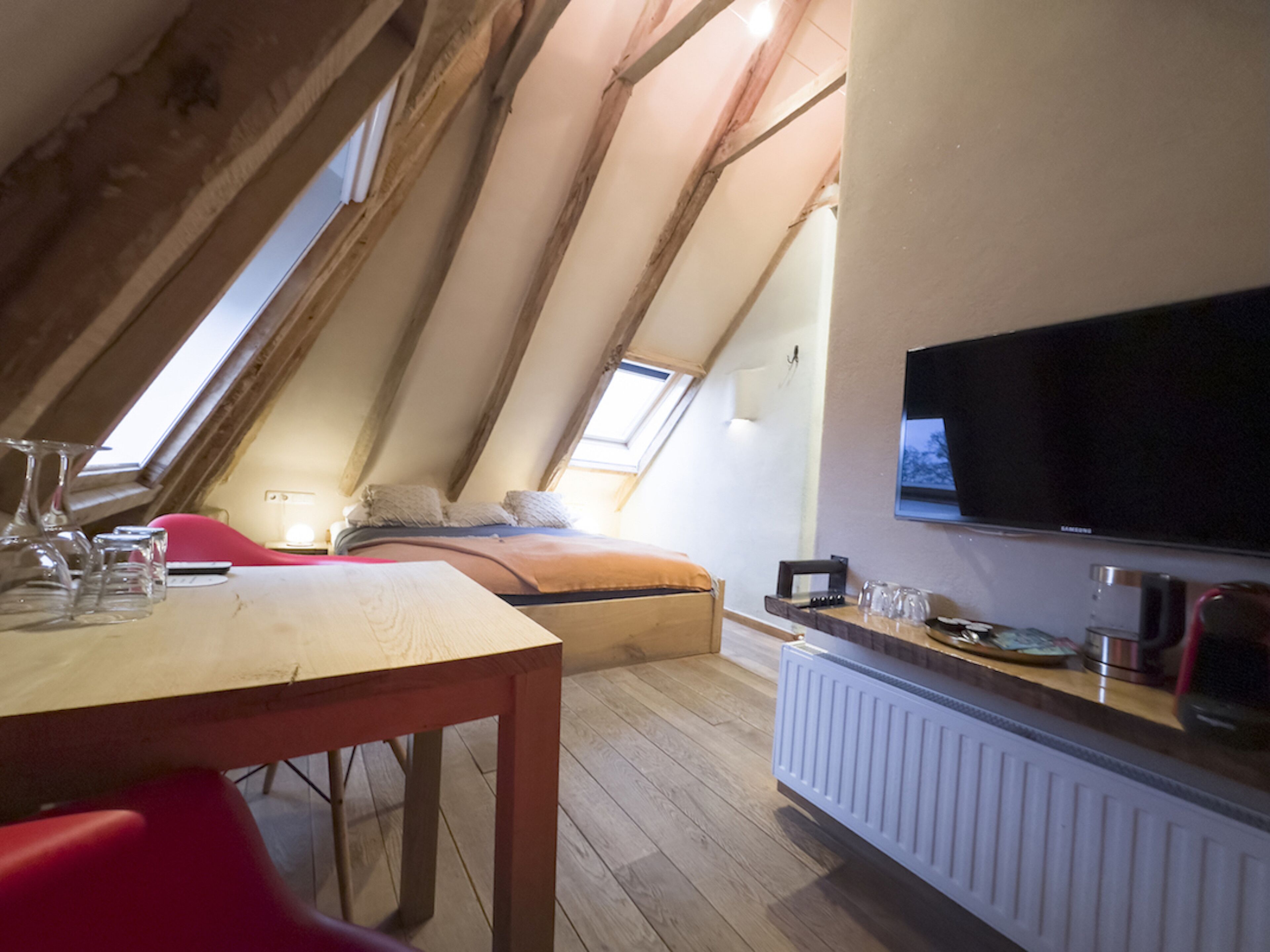Une pièce avec un plafond en pente, un lit, une télévision et une table avec des verres.