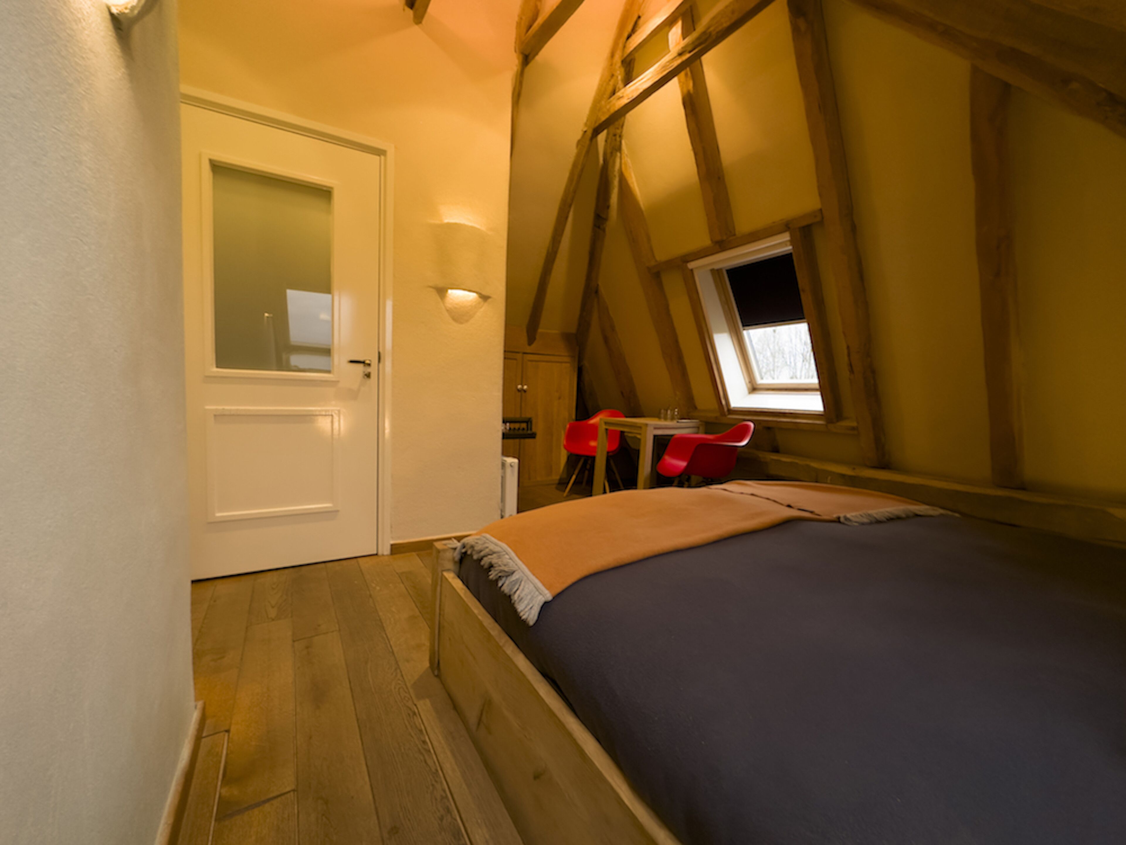 Un dormitorio con cama, puerta, ventana y una silla roja.