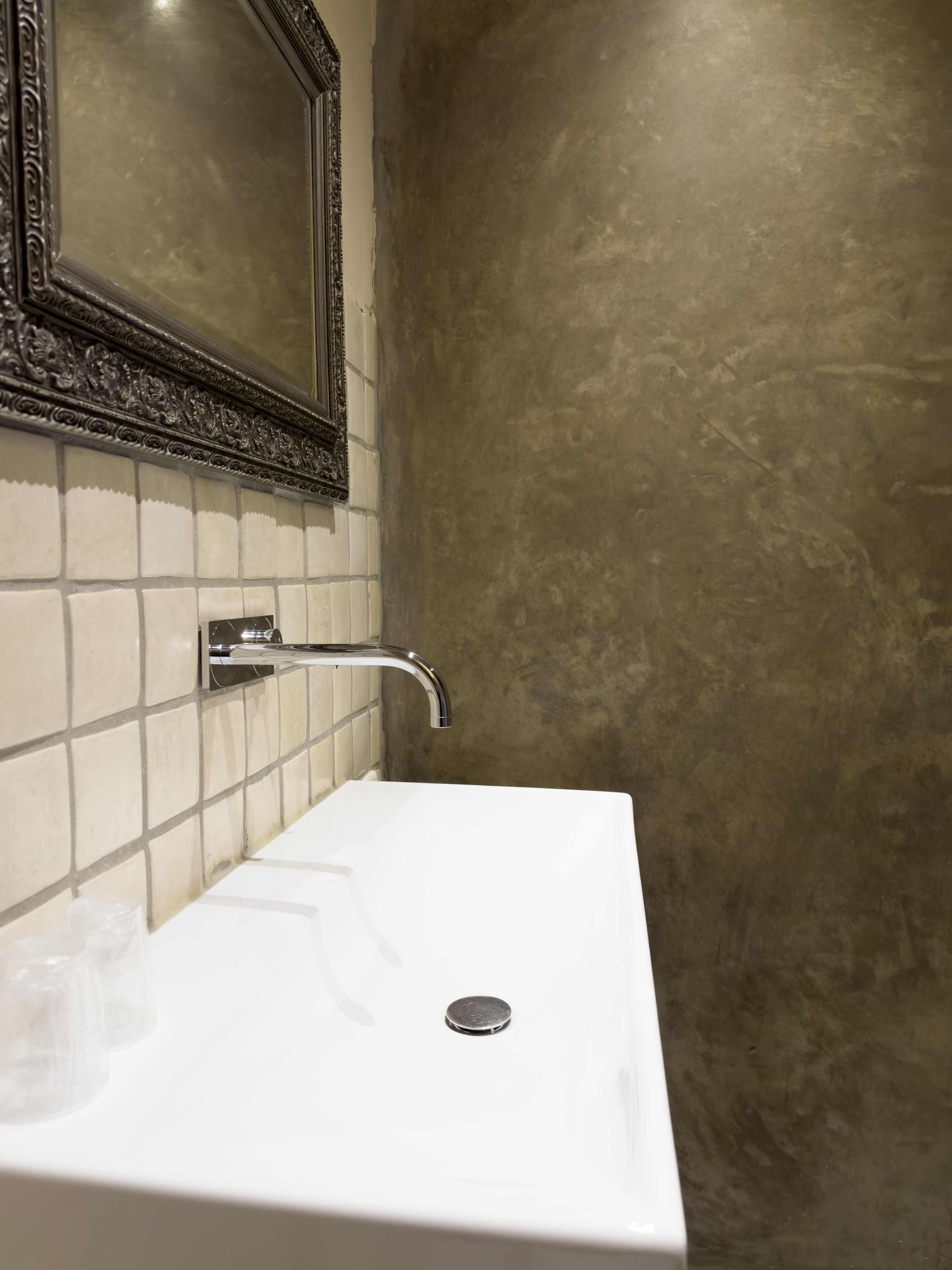 A bathroom with a white sink, a mirror with an ornate frame, and a textured wall.