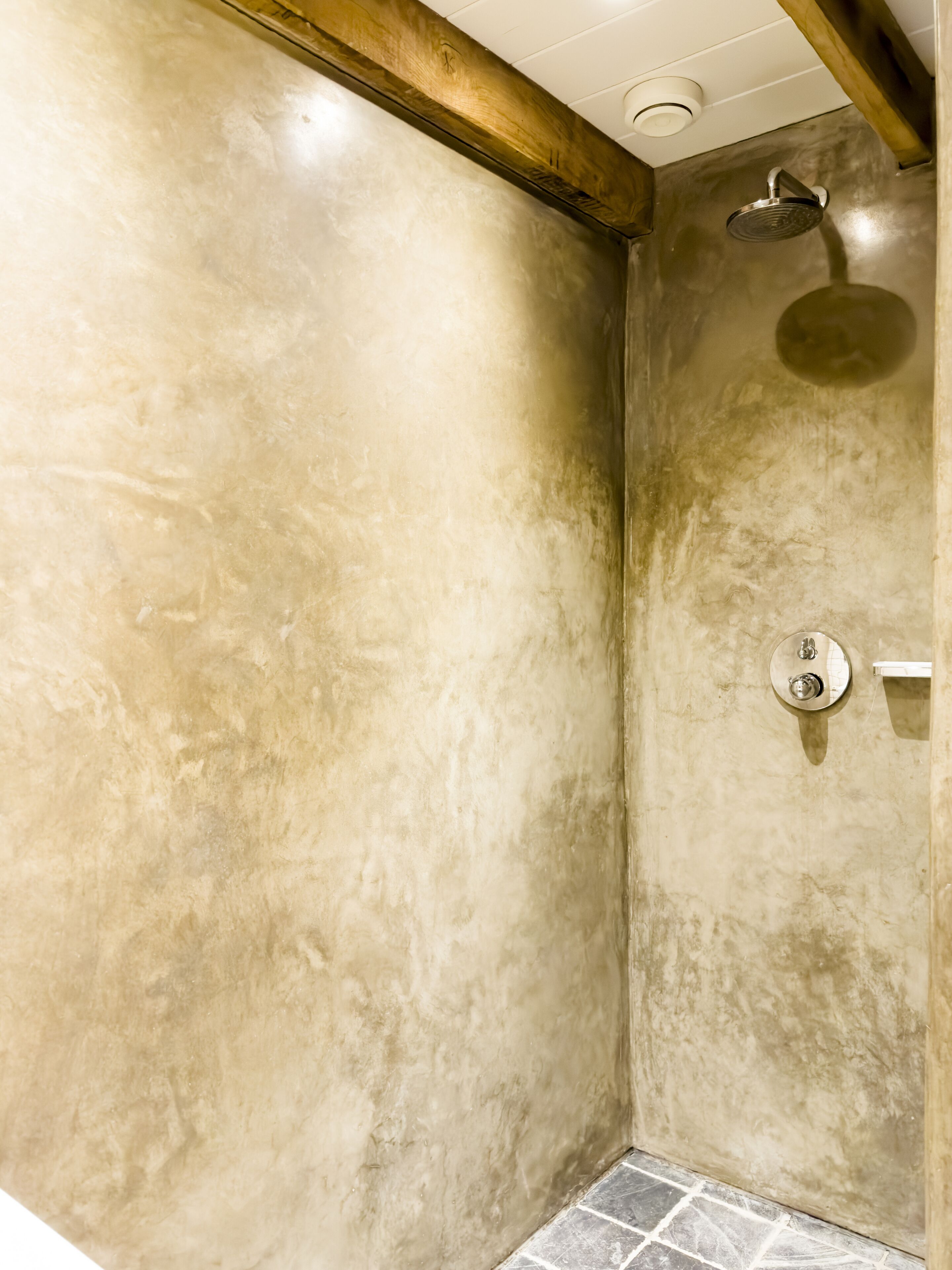 A bathroom with a shower, tiled floor, and a wooden ceiling beam.