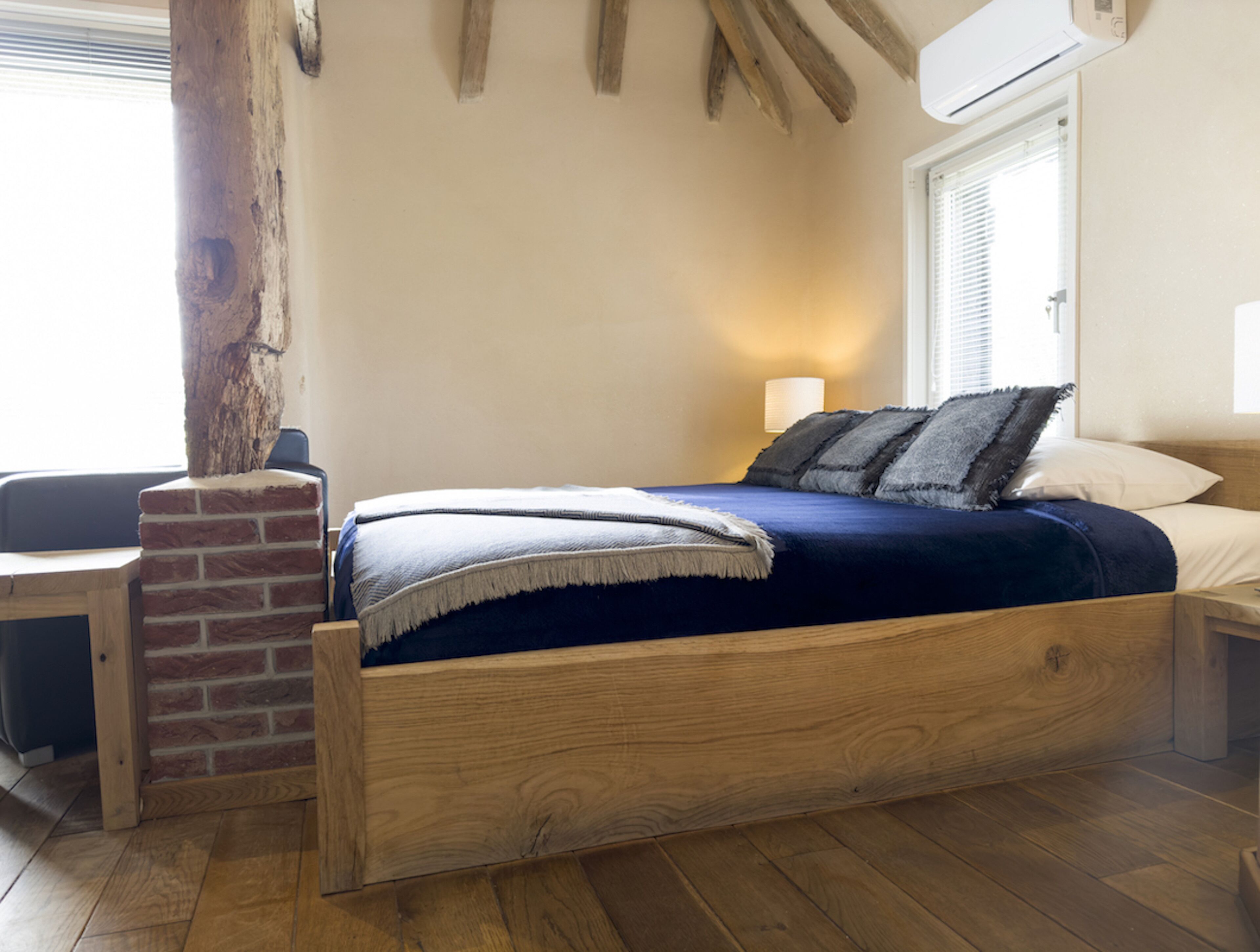 Un lit en bois, un mur en briques, une table de chevet et une lampe.