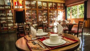 Zona pranzo con tavoli apparecchiati per quattro persone, circondata da scaffali colmi di libri.
