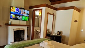 Habitación de hotel con chimenea, televisor mostrando opciones de películas, espejo y toallas ordenadas sobre la cama.