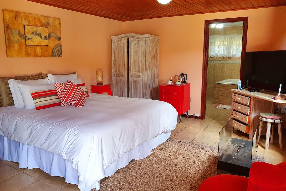 Een slaapkamer met een groot bed, een rode nachtkastje, een houten garderobe, een bureau met stoel en een televisie.