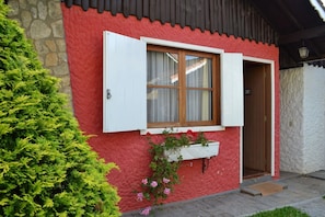 Un bâtiment rouge avec des volets blancs, une porte en bois et une fenêtre avec des rideaux.