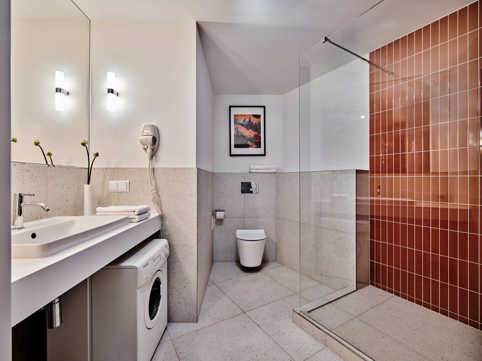 Un baño moderno con lavamanos, espejo, secador de pelo, inodoro y zona de ducha.