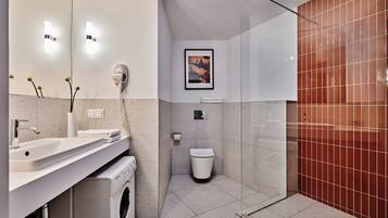 Un baño moderno con lavamanos, espejo, secador de pelo, inodoro y zona de ducha.