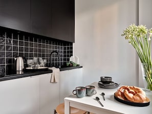 A modern kitchen with black tiles, a kettle, cups, and a loaf of bread on the counter. - Media Park (Warsaw)