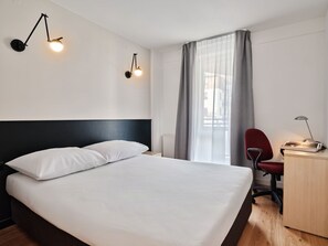 A hotel room with a bed, a desk, a chair, and two wall-mounted lamps. - Media Park (Warsaw)