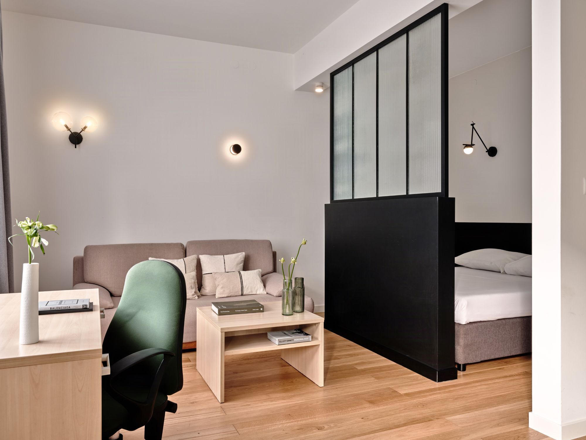 A modern hotel room with a bed, a desk, a sofa, and a small coffee table.