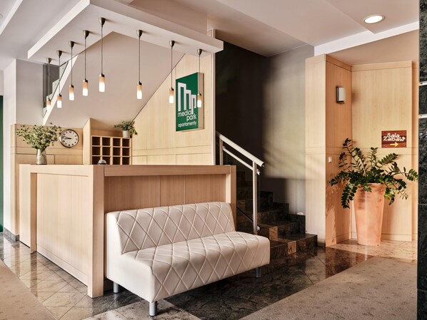 A modern reception area with a sofa, a clock, a sign for 'Media Park Apartment', and a staircase. - Media Park (Warsaw)