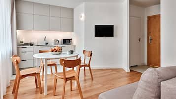 Una cocina moderna con armarios blancos, una mesa de comedor con sillas, un televisor de pantalla plana en la pared y una puerta de madera.