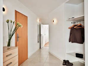 A modern hallway with a wooden door, a glass vase with flowers, a white wardrobe with hangers, and a pair of shoes on the floor. - Media Park (Warsaw)