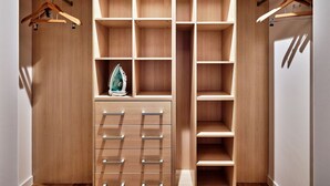 Ein begehbarer Kleiderschrank mit mehreren Regalen und Platz zum Aufhängen, inklusive integriertem Bügelbrett und einem hängenden Bügeleisen.