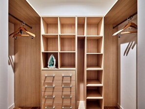 A walk-in closet with multiple shelves and hanging space, featuring a built-in ironing board and a hanging iron. - Media Park (Warsaw)